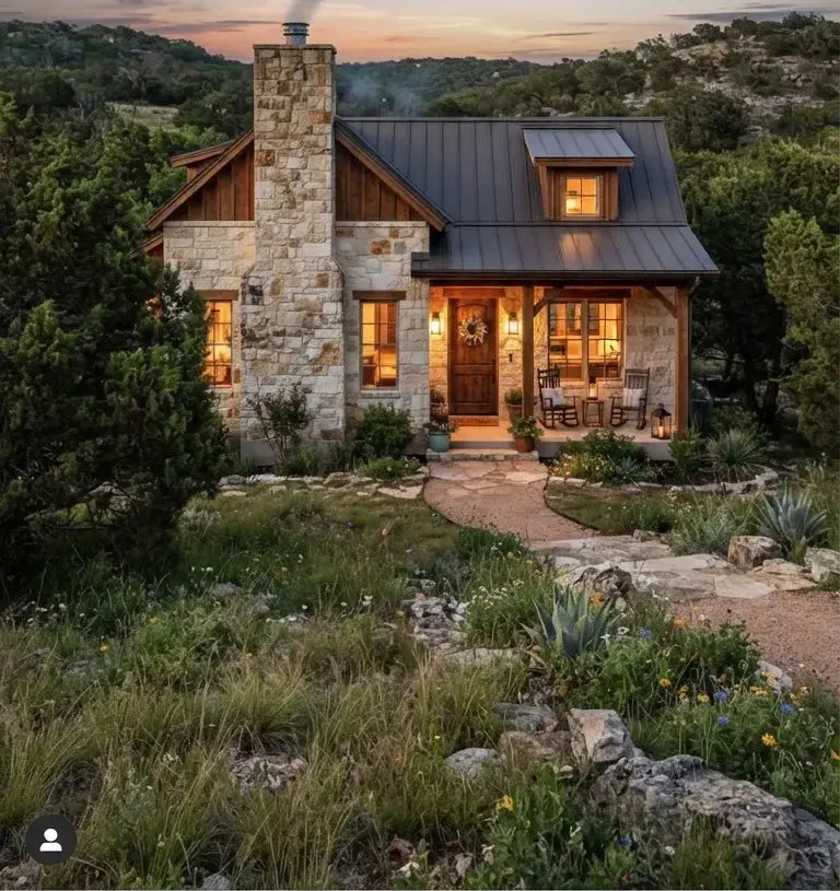 Charming stone residence on Mount Gainor Way set in quiet cedar hilltops with wild grasses, stone chimney, and warm amber outdoor lighting.