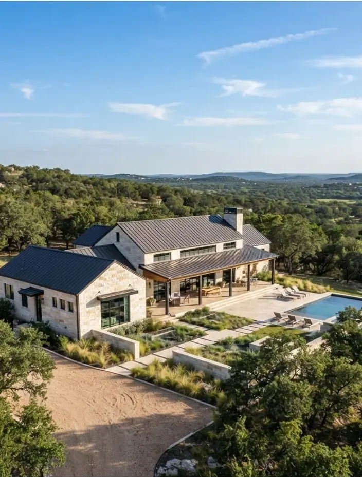 Modern architectural ranch estate surrounded by rolling cedar and live oak trees under bright Texas afternoon sky in Blanco County.